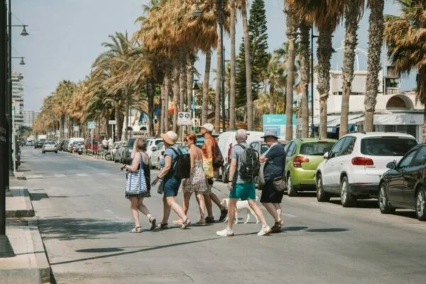 Tourists crossing a palm-lined street in Málaga, Spain, during a sunny day.