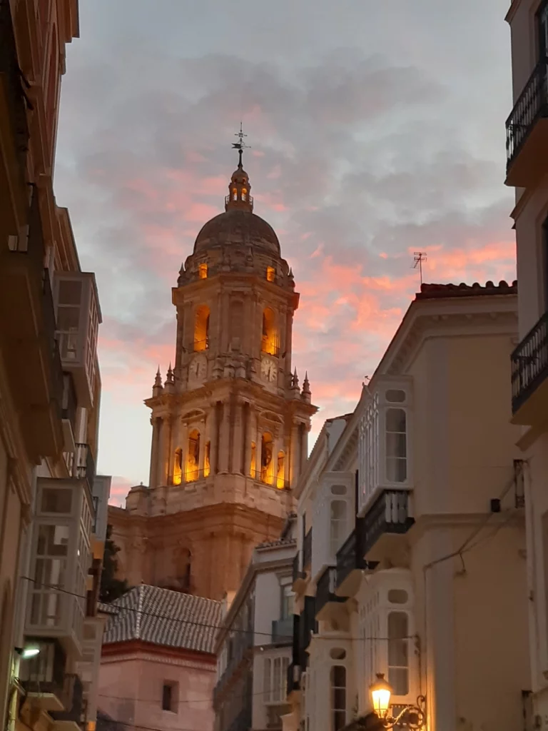 View of Málaga Cathedral at sunset, with its illuminated tower rising above historic city streetsView of Málaga Cathedral at sunset, with its illuminated tower rising above historic city streets